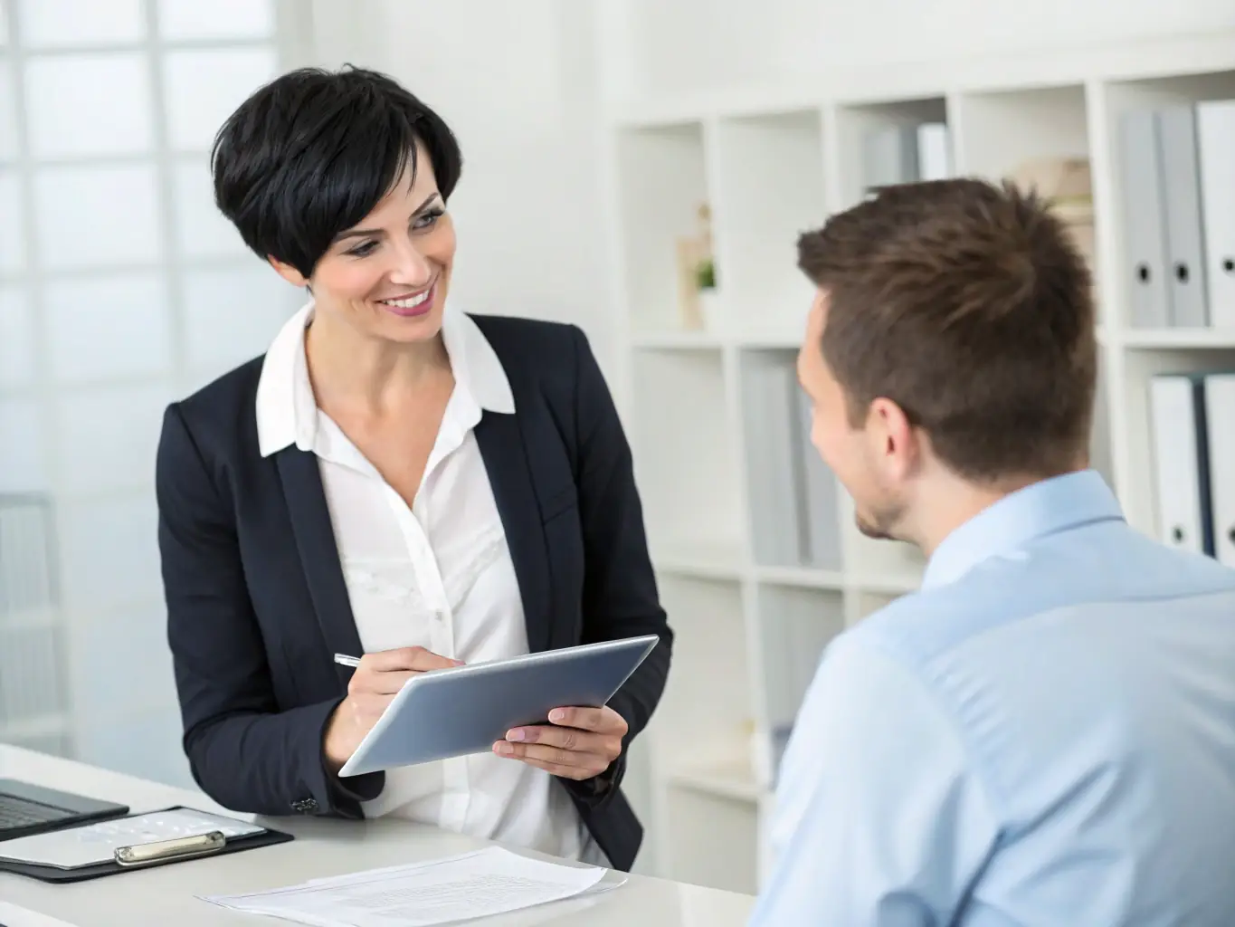 A professional recruiter is interviewing a candidate in a modern office setting. The recruiter is taking notes while the candidate is confidently answering questions. The scene conveys professionalism and attention to detail.